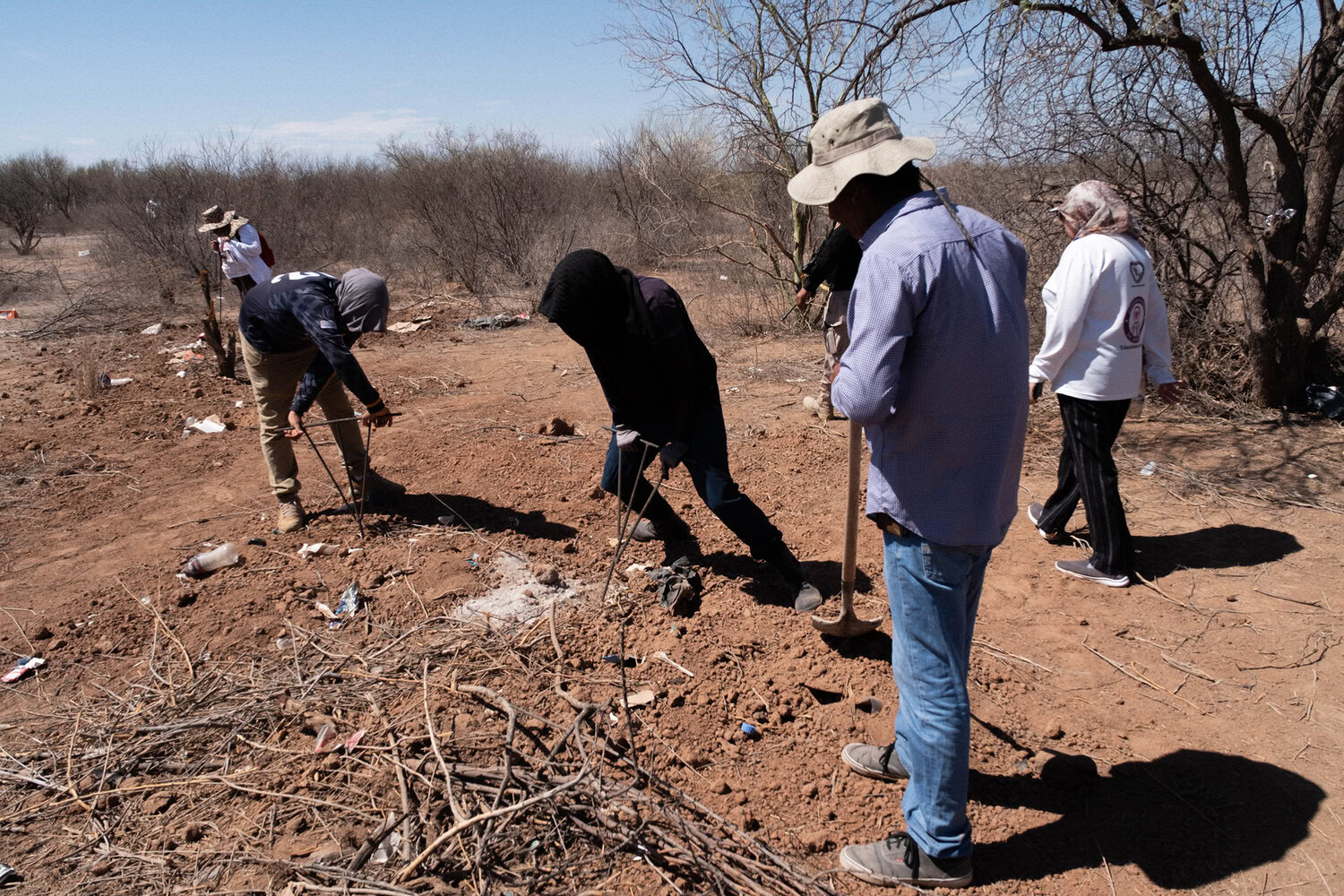 Six people wearing hats and long sleeves work on a dry, barren landscape, clearing debris and tending to the land.